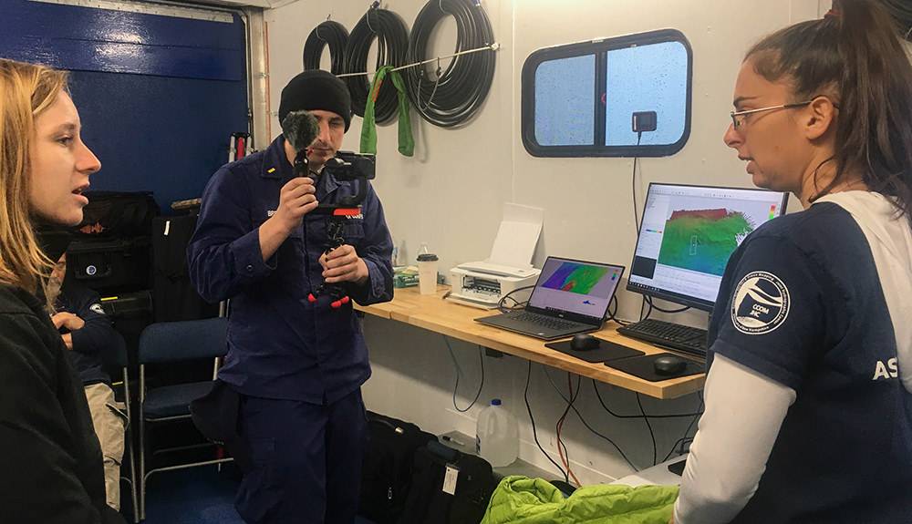 Ein wesentlicher Bestandteil der täglichen Arbeit des Expeditionsteams war die Aufklärung und Öffentlichkeitsarbeit, die hier gezeigt wird, wenn die Teammitglieder live vom Mission Control Van übertragen werden. Live-Übertragungen beinhalteten direkte Verbindungen zu Klassenzimmern und über Facebook Live. Sie können archivierte Sendungen über die Facebook-Seite des Office of National Marine Sanctuaries anzeigen. (Foto: Ocean Exploration Trust)