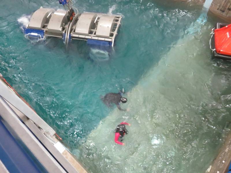 O mergulhador (em preto) ajuda o trabalhador offshore (em vermelho) a alcançar a segurança do bote salva-vidas à direita da imagem. (Foto: Tom Mulligan)