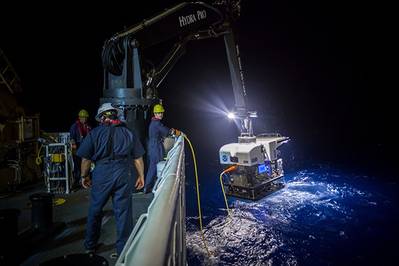 Crew members aboard a NOAA ship in 2016 use a crane to hoist a remotely operated vehicle (ROV) from the water at night. NOAA is seeking proposals for new ocean survey ships that can deploy a variety of equipment, including ROVs like the one pictured here. Credit: NOAA