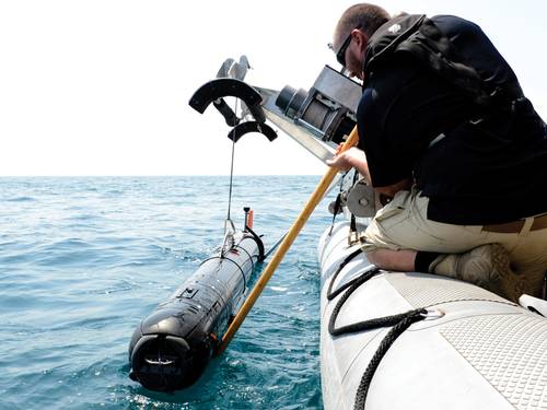 A civilian contractor steadies a M18 Mod 2  Kingfish Unmanned  Underwater Vehicle (UUV) as it is lifted with a crane onto the deck of an  11-meter rigid-hull  inflatable boat.  (U.S. Navy photo by Mass Communication Specialist 2nd Class Blake Midnight/Released)