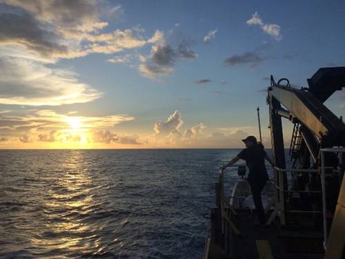 Emily Narrow, mission videographer, enjoys the sunset over the Pacific Ocean from the back deck of NOAA Ship Okeanos Explorer during the NOAA Ocean Exploration mission: Discovering the Deep: Exploring Remote Pacific Marine Protected Areas in 2017. Credit: NOAA Ocean Exploration