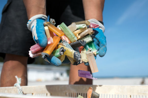 A marine debris team member gathers a handful of disposable cigarette lighters picked up at a beach cleanup site. (NOAA)