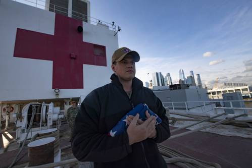 U.S. Navy file photo of Aviation Boatswain's Mate 2nd Class Justin Cosgrove participating in morning colors aboard the hospital ship USNS Comfort (T-AH 20) while the ship is moored in New York City in support of the nation™s COVID-19 response efforts. (U.S. Navy photo by Mass Communication Specialist 2nd Class Sara Eshleman)