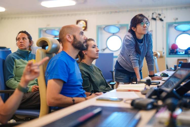 In the Computer Electronics Lab on board Research Vessel Falkor (too), the science team assembles to see the CTD data during the initial deployment of the CTD rosette. "CTD" stands for conductivity, temperature, and depth, and refers to a package of electronic devices used to detect how the conductivity and temperature of water changes relative to depth.
Credit: Alex Ingle / Schmidt Ocean Institute