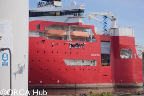 The Imperial College London drone demonstrating autonomous UAV sensor placement on a wind turbine at the ORE Catapult facility in Blyth. The drone is equipped with a winch-tethered magnet and passive wheels capable of perching on, and sliding along, both vertical and horizontal surfaces.