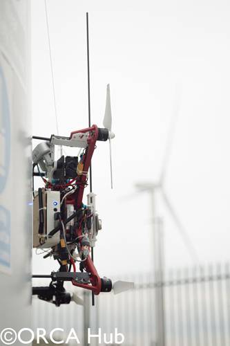 The Imperial College London drone demonstrating autonomous UAV sensor placement on a wind turbine at the ORE Catapult facility in Blyth. The drone is equipped with a winch-tethered magnet and passive wheels capable of perching on, and sliding along, both vertical and horizontal surfaces.