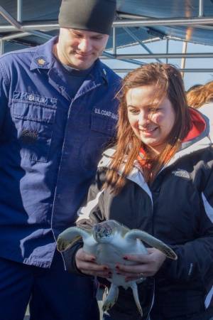 Petty Officer 2nd Class Mitchel Heavilin, a gunner's mate aboard Coast Guard Cutter Kodiak Island out of Atlantic Beach, N.C., looks on as a civilian passenger prepares to release a sea turtle from cutter Kodiak Island off the the North Carolina coast, Dec. 15, 2014. The Coast Guard, in cooperation with the North Carolina Resources Commission, released a total of 19 rehabilitated sea turtles into the Gulf Stream off the coast of North Carolina. (Photo by Kevin E. Geraghty)
