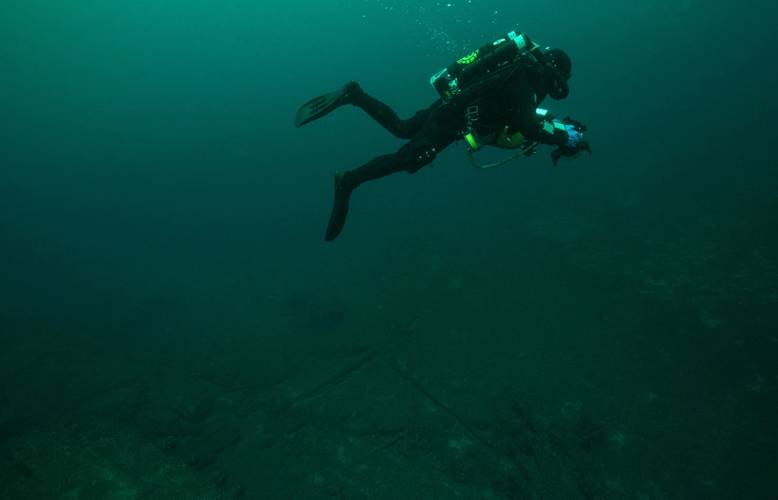 Phase IV started with a series of ‘work-up’ dives used to practice technical diving techniques and refine the photogrammetric imagery acquisition protocols before visiting deeper sites. Here, NOAA Diver Joe Hoyt swims above the debris field off the stern of wooden bulk carrier New Orleans. He maintains a consistent altitude off the bottom, necessary to ensure broader coverage of the debris field features as the relate to the main vessel remains. (Credit: NOAA, Thunder Bay National Marine Sanctua