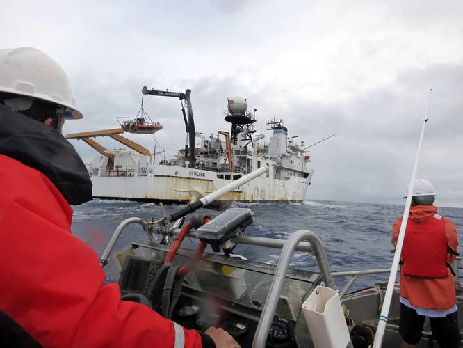 A small boat approaches the NOAA Ship Hiʻialakai, as another boat that just returned is carefully placed in its 'cradle' with a crane. (Photo: NOAA Fisheries)
