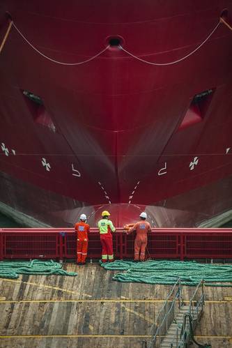 DOF subsea workers stand on the deck facing the hull of a massive DOF Subsea offshore vessel.  (Photo courtesy of DOF Subsea)